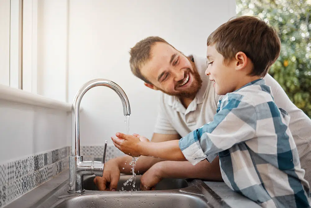 father helping son wash hands in kitchen sink